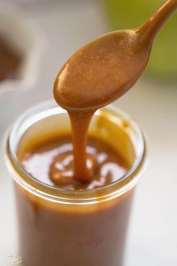 Caramel sauce dripping off spoon into glass container.