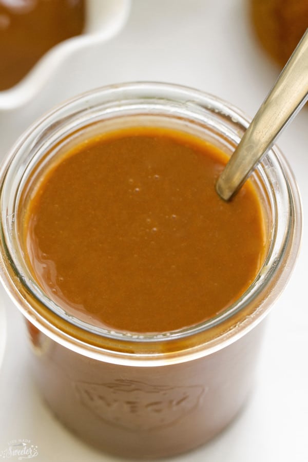 Glass jar of easy Caramel Sauce with a silver spoon.