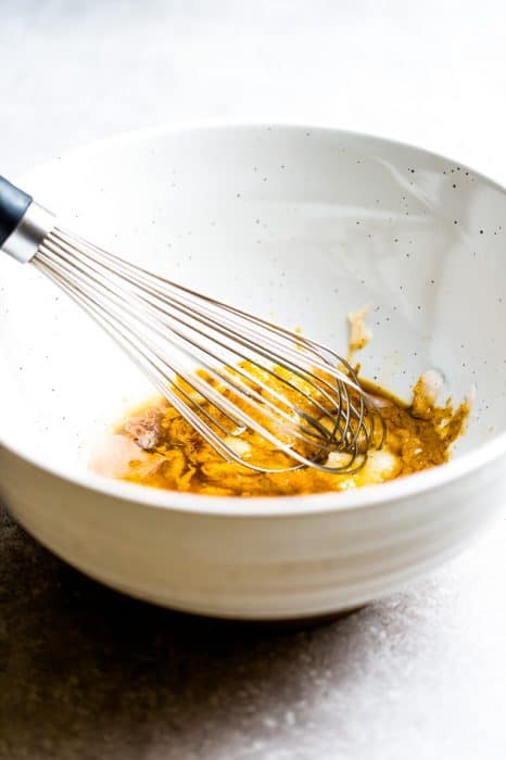 Side view of ingredients to make Soft and Chewy Granola Bars in a white bowl with a whisk