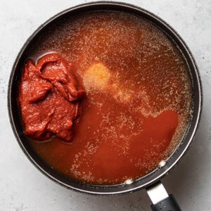 Ingredients side-by-side in a saucepan to make homemade ketchup: tomato sauce, tomato paste, coconut aminos, water and spices