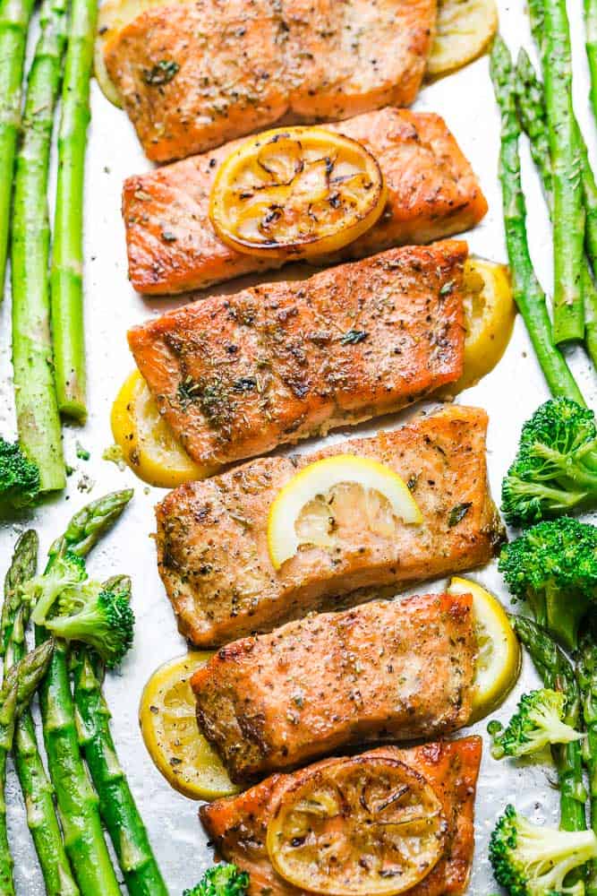 Close up of roasted lemon butter salmon fillets on a baking sheet with lemon slices and roasted veggies on the side