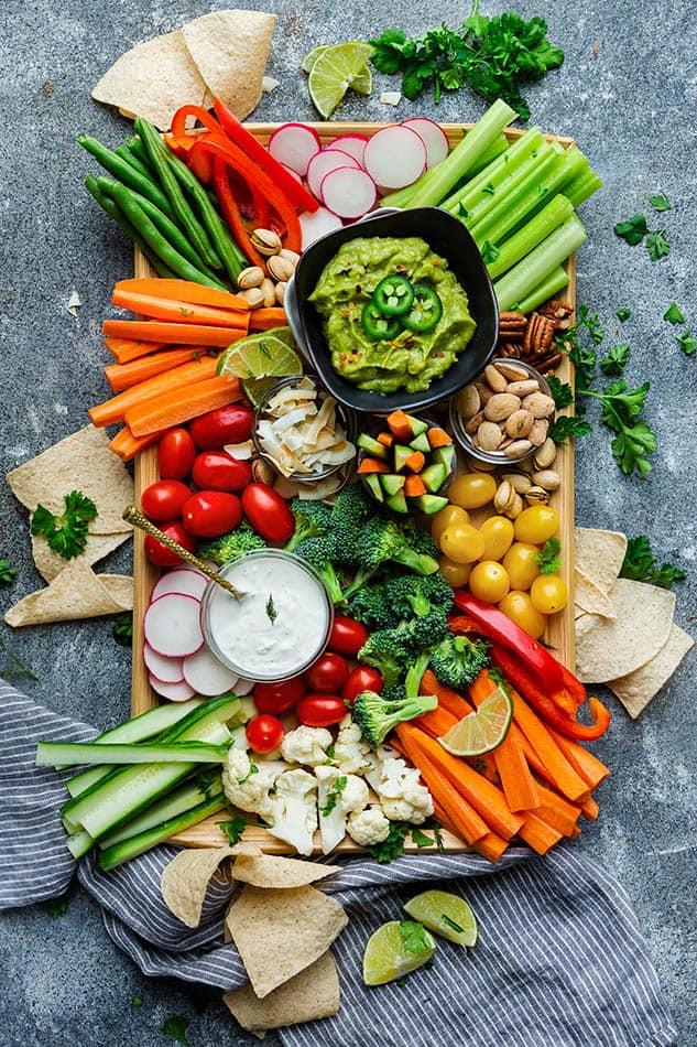 Top view of paleo veggie platter on a wooden tray on a grey background with Siete tortilla chips