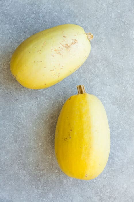 Two whole spaghetti squash on a gray background