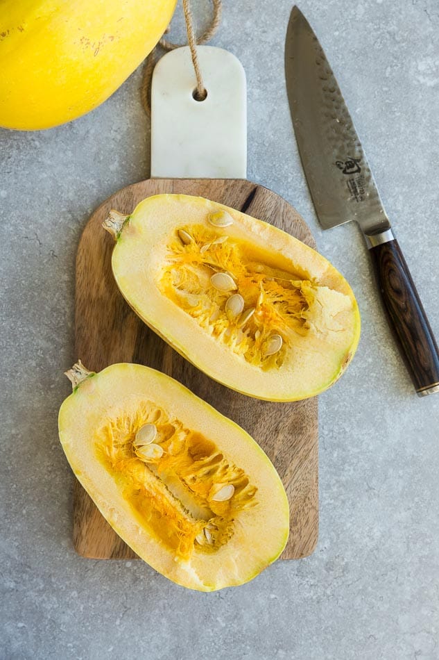 Overhead view of two raw spaghetti squash halves on a wooden cutting board