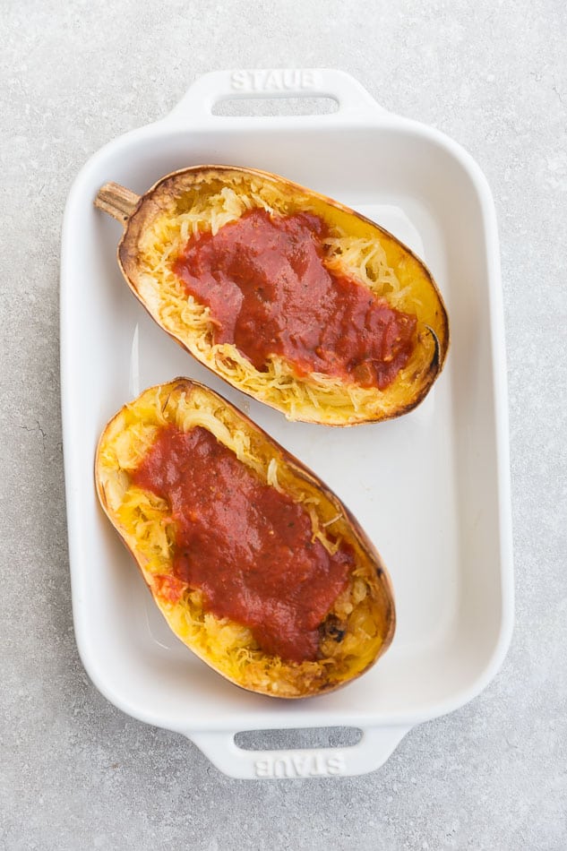 Overhead view of spaghetti squash halves with tomato sauce in a baking dish