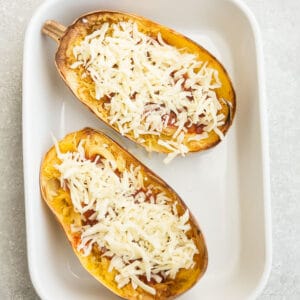 Overhead view of spaghetti squash halves with tomato sauce and cheese in a baking dish