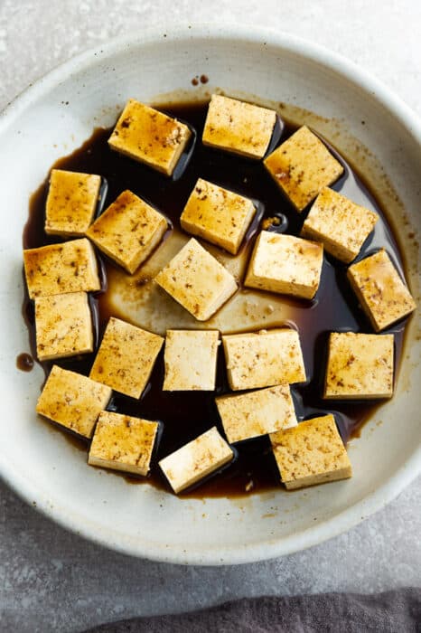 The top view of tofu cubes marinating in coconut aminos and the rest of the seasonings in a shallow bowl
