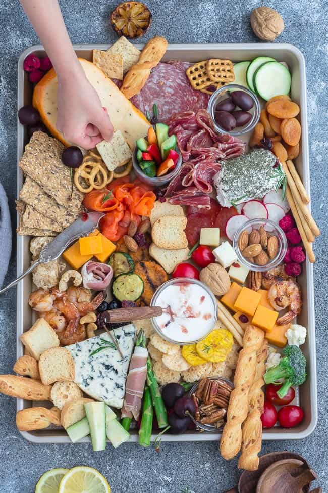 A hand reaching to grab a cracker from a cheese board built on a baking sheet