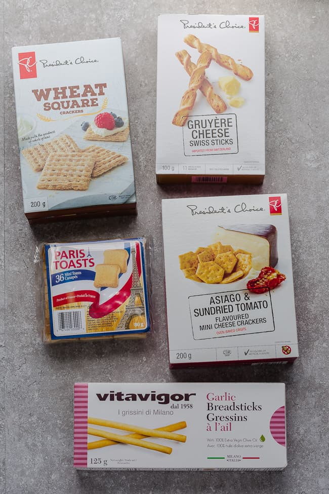 Five boxes of crackers: wheat square crackers, gruyère cheese Swiss stick, mini toasts, asiago and sundried tomato flavored mini cheese crackers, and garlic breadsticks 