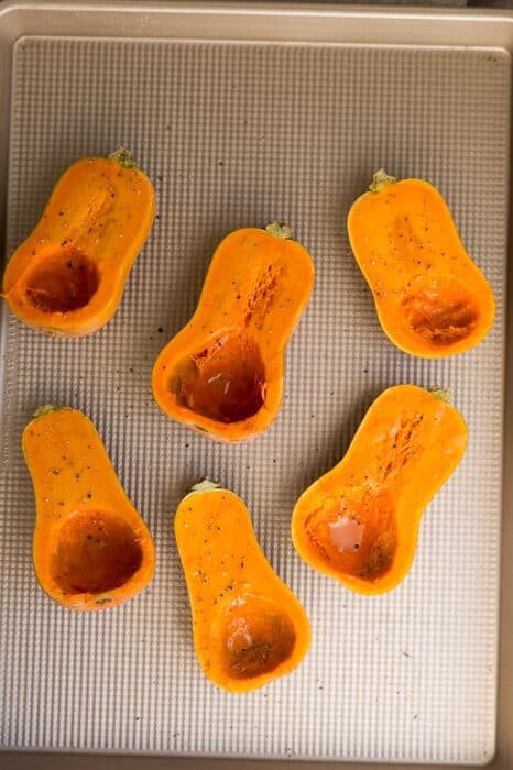 Top view of 6 honeynut squash halves on a rimmed baking sheet