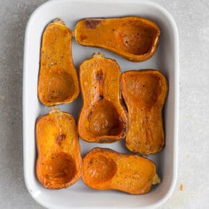 Top view of 6 honeynut squash halves in a white rectangle casserole dish