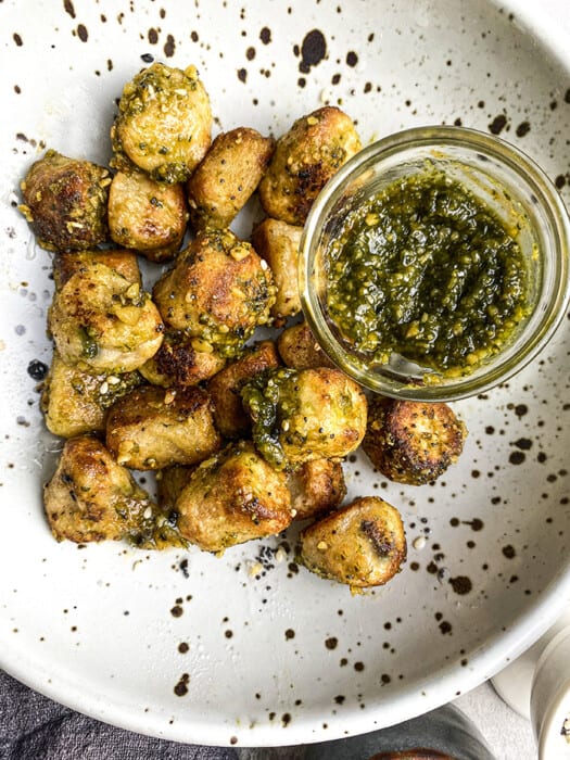 Cauliflower Gnocchi on a White and Black Plate with a Dish of Pesto Sauce
