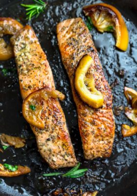 Top view of perfect pan seared salmon in a cast iron skillet with lemon slices