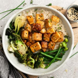Top view of crispy air fryer tofu in a white bowl with cauilflower rice, broccoli, bok choy and green beans