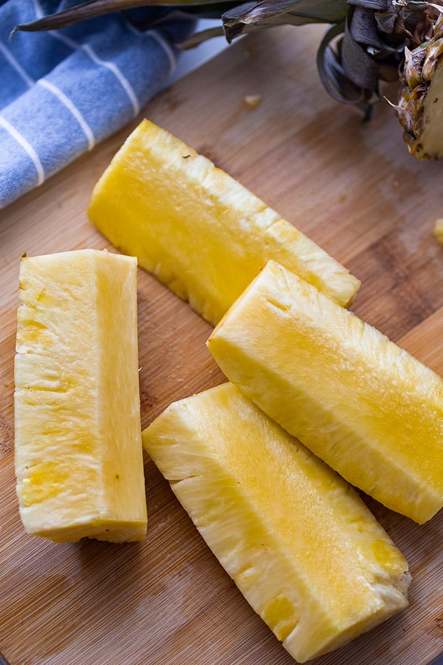 Overhead image of pineapple cut into vertical spears on wooden cutting board.