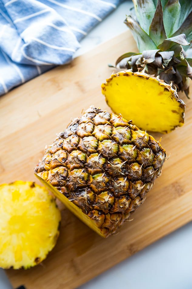 Top view of a pineapple with the top and bottom ends cut on a wooden cutting board