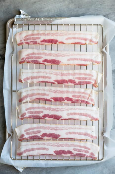 Top view of 7 raw bacon on a cookie rack on top of parchment paper