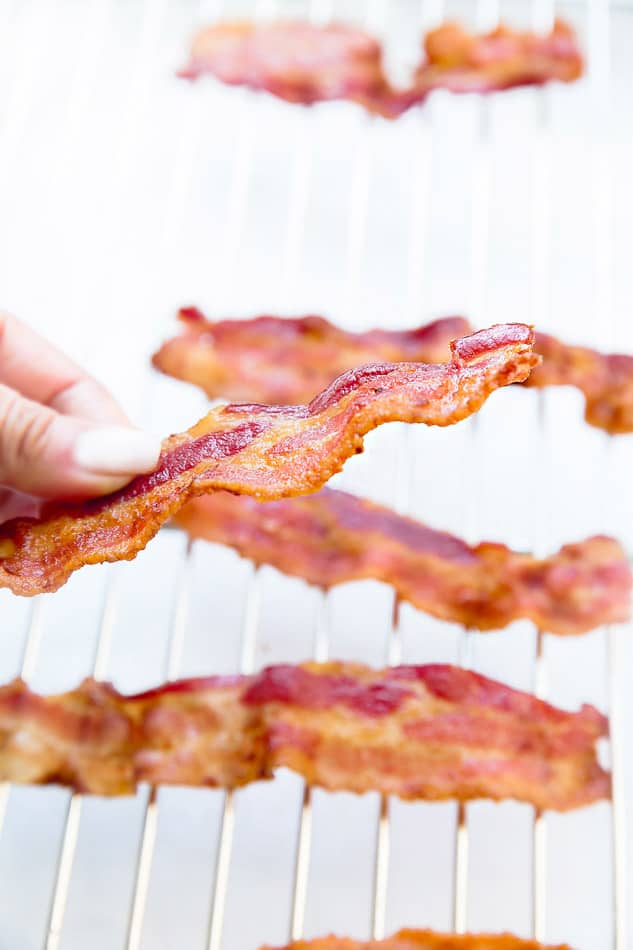 Side view of a hand holding crispy oven baked bacon