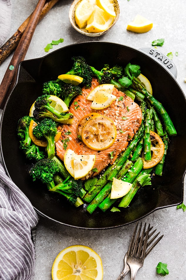 A pan-seared salmon fillet in a cast-iron skillet with broccoli and asparagus