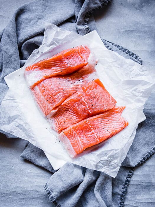 Four raw salmon fillets sitting on a stack of pieces of parchment paper
