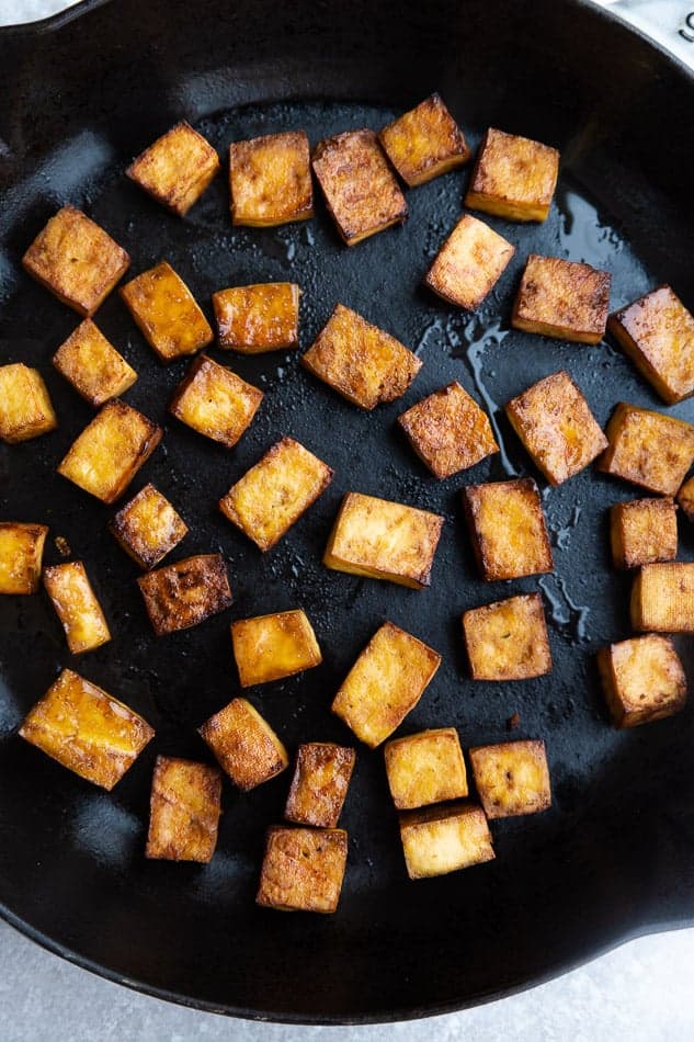 Crispy cubes of pan-fried tofu in a skillet with a small amount of oil
