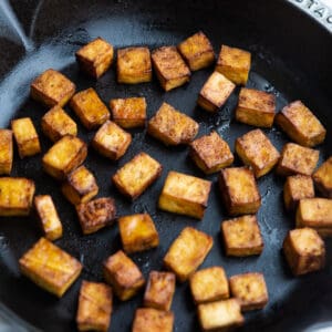Side view of pan fried tofu on a cast iron skillet