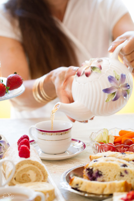 Tea being poured into a cup on a table with treats for a tea party