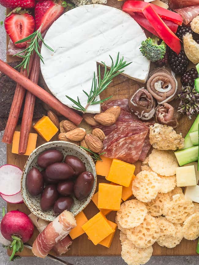 Close up of a cheese board with a round of brie, a bowl of kalamata olives, and some fresh strawberries