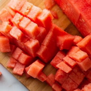 Top view of half of watermelon without the rind cut into cubes on a wooden cutting board