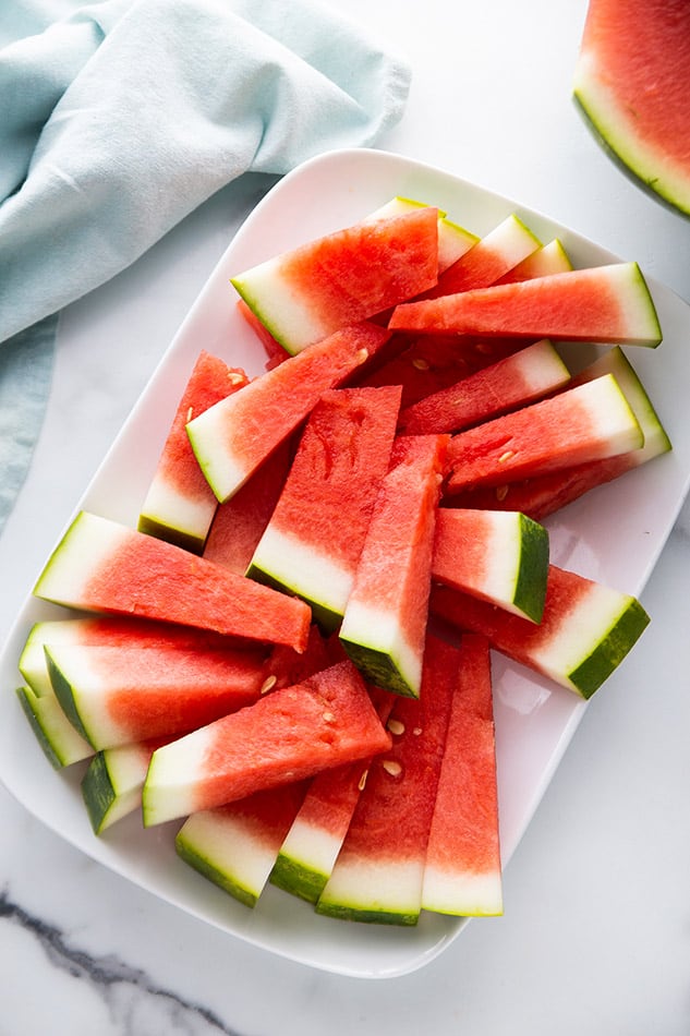 Overhead view of cut watermelon on white serving dish.