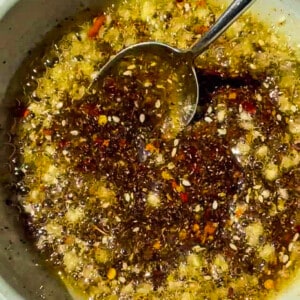 Hot oil getting poured over spices in a bowl: chili flakes, garlic, salt, ginger and more.
