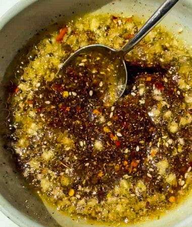 Hot oil getting poured over spices in a bowl: chili flakes, garlic, salt, ginger and more.