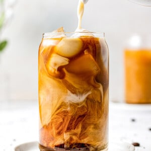 Non-dairy milk being poured from a pitcher into a glass of homemade cold brew coffee