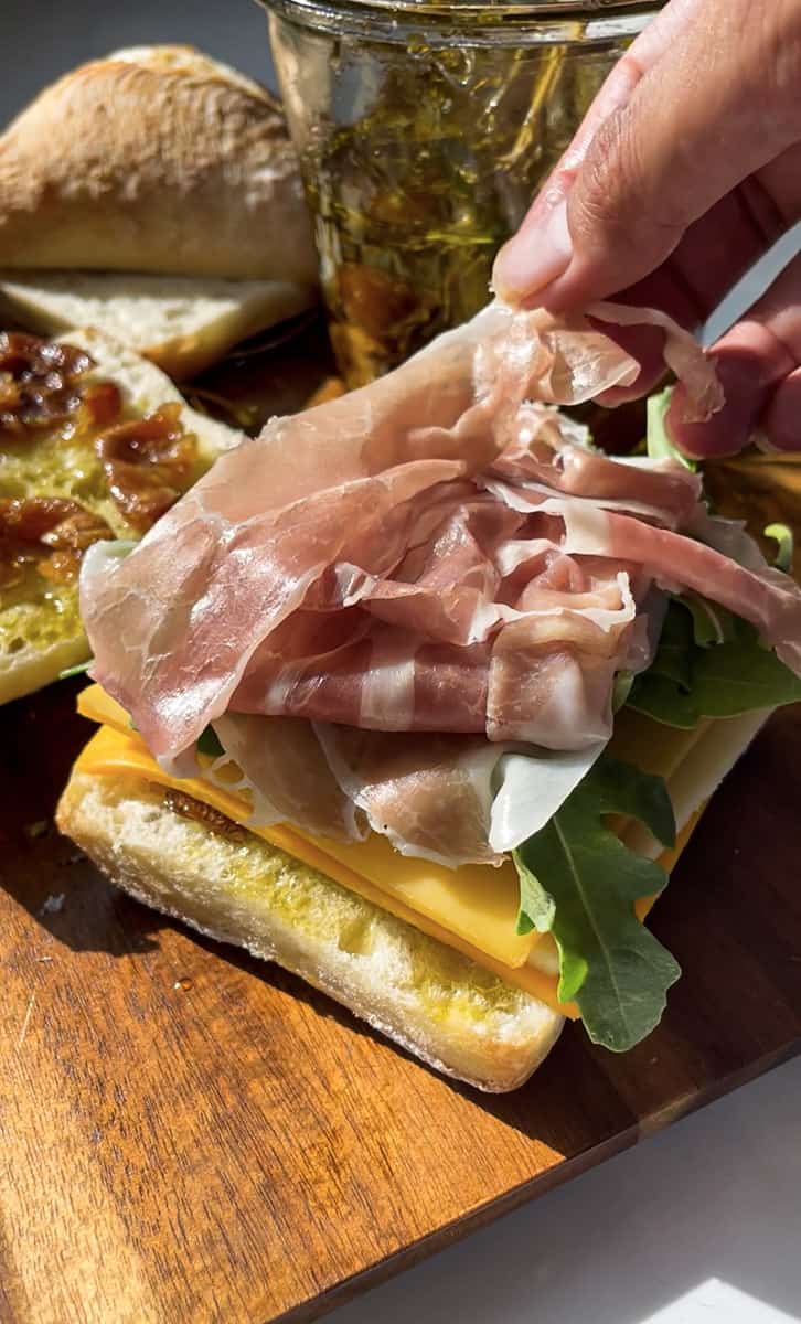 An open-faced sandwich with prosciutto, arugula and cheese on a wooden cutting board