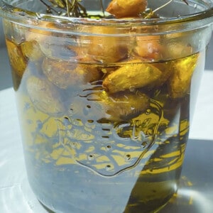 A canning jar filled with roasted garlic cloves and herbs covered in oil