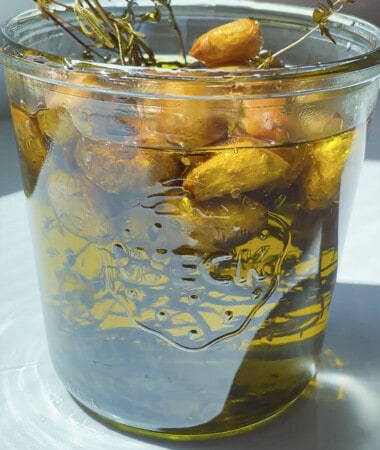 A canning jar filled with roasted garlic cloves and herbs covered in oil