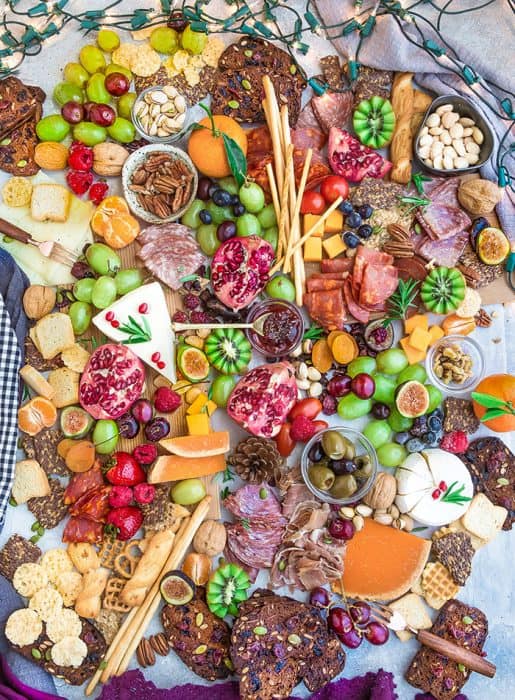 Top view of a holiday cheese board with a variety of crackers, nuts, fruit, meats, and cheeses
