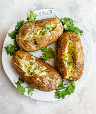 Overhead view of 3 baked potatoes cut open on a plate with fresh herbs