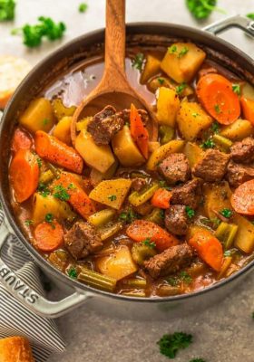 An entire pot of classic beef stew in a grey dutch oven with a wooden spoon