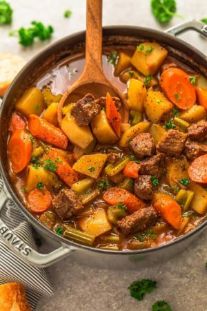 An entire pot of classic beef stew in a grey dutch oven with a wooden spoon