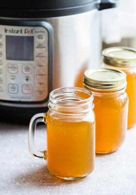 Side view of pressure cooker and mason jars filled with Instant Pot Chicken Stock