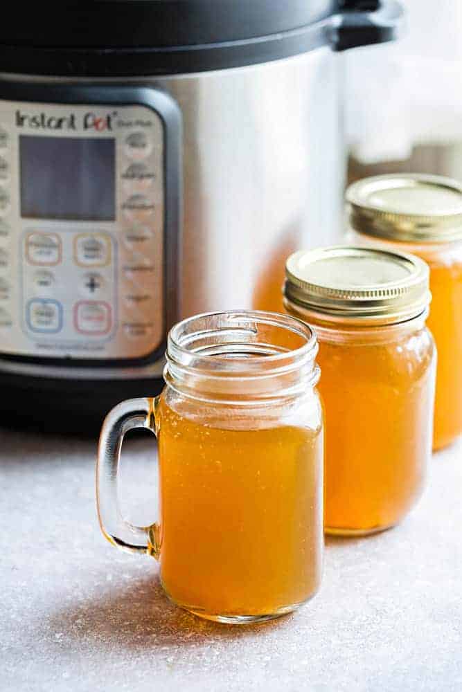 Side view of pressure cooker and mason jars filled with Instant Pot Chicken Stock