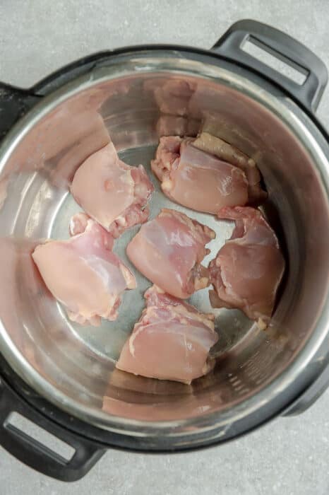 Top view of raw chicken thighs in an Instant Pot pressure cooker instant pot on a grey background