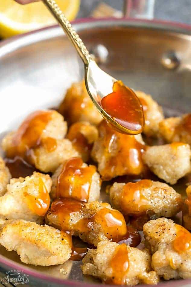 Honey lemon sauce being spooned over breaded chicken pieces in a skillet