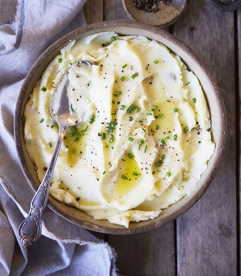 Top view of mashed potatoes in a serving bowl topped with black pepper and chives