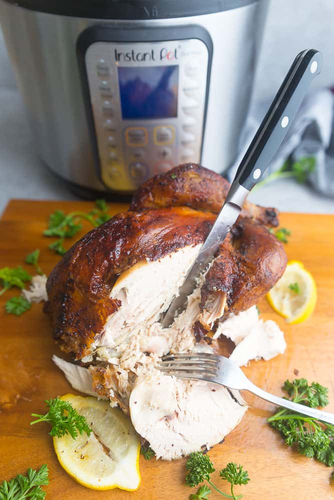 carving knife and fork slicing a whole chicken next to the Instant Pot it was cooked in