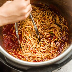 Spaghetti and Meat Sauce Being Stirred Around with Tongs in a Pressure Cooker