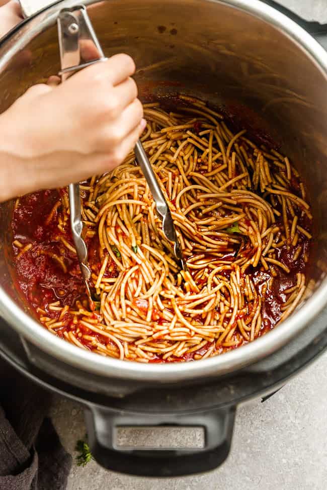 Spaghetti and Meat Sauce Being Stirred Around with Tongs in a Pressure Cooker