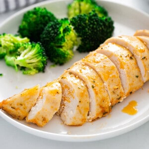 Landscape shot of one serving of oven baked chicken breast sliced with a side of steamed broccoli on a white plate