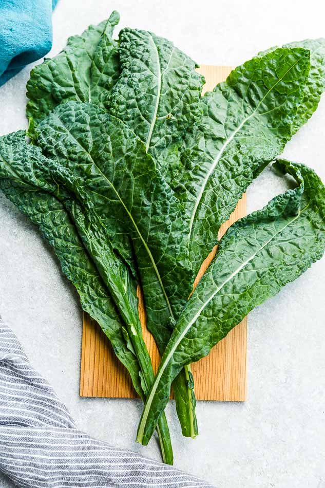 Six fresh kale leaves laid out on a wooden board on top of a granite kitchen counter